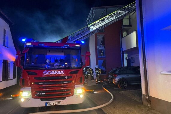 Feuerwehr beim Löschen eines Wohnungsbrands, Alarmstimmung, Einsatzkräfte und beschädigtes Gebäude sichtbar.