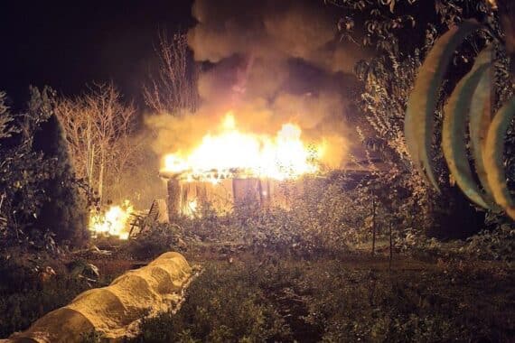 Gartenanlage mit brennender Laube, Feuerwehr im Einsatz, zerstörter Toilettenbereich und Garage.