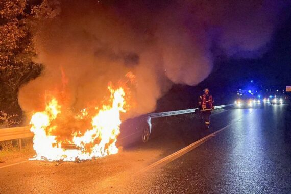 PKW in Vollbrand, Feuerwehr im Einsatz, Rauch und Löscharbeiten auf der Straße.