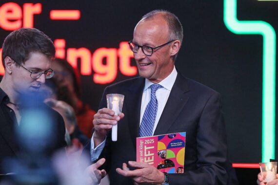 Friedrich Merz singt mit Menschen in Halle, umgeben von Kerzenlicht und Applaus.