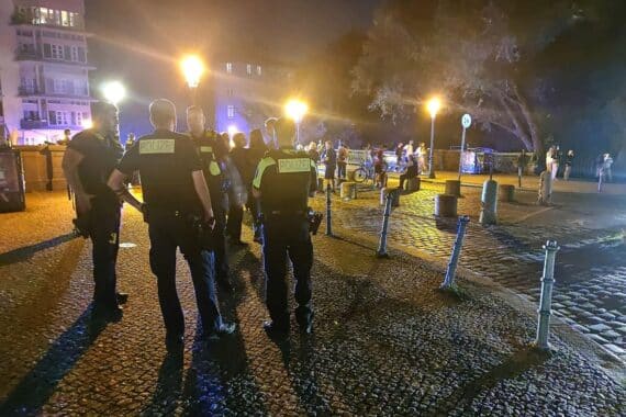 Polizisten kontrollieren eine Gruppe in einer belebten Innenstadt, Sicherheitsmaßnahmen im Fokus.