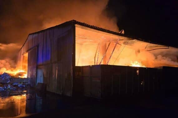 Brand in Wertstoff-Sortierhalle mit Feuerwehr im Einsatz, starker Rauch und Gebäudeschaden sichtbar.