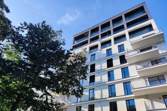 Visualisiere einen Baukran vor einem Neubau, der bezahlbaren Wohnraum symbolisiert, mit Menschen.