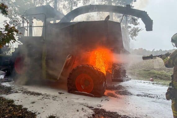 Maishäcksler brennt lichterloh auf einem Feldweg, Feuerwehr kämpft gegen die Flammen.