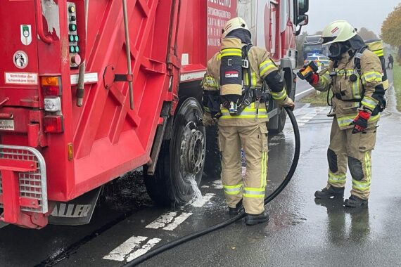 Müllwagenbrand auf Bundesstraße: Feuerwehr löscht Flammen, keine Verletzten, Straße gesperrt.