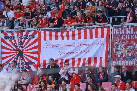 Zwei Gruppen von Fußballfans marschieren friedlich zum Stadion, begleitet von Sicherheitskräften.