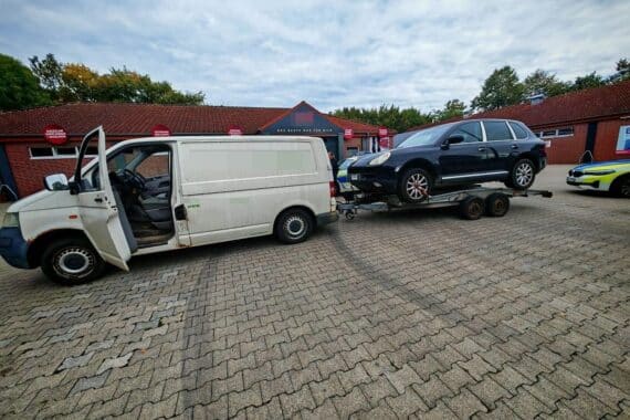 Überladener Kleintransporter mit SUV-Anhänger und kontrollierenden Polizisten auf Autobahn.