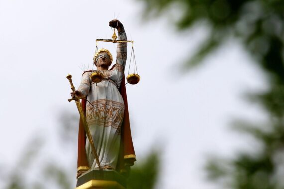 Gerichtssaal mit Justitia-Symbolik, Anklage wegen PKK-Mitgliedschaft, angeklagter Mann im Fokus.