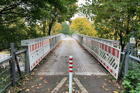 Beschädigte Fußgängerbrücke mit abgeschnittenen Stahlseilen, Absperrgitter sichtbar, Polizei ermittelt.