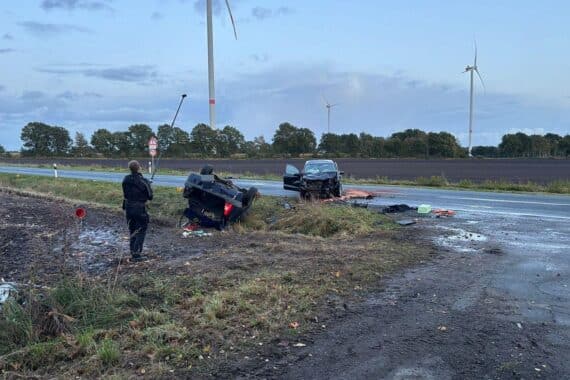 Unfallstelle mit Polizei und Rettungskräften, beschädigte Fahrzeuge auf nasser Straße.