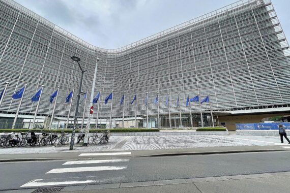 EU-Fahnen wehen vor Brüssel, symbolisieren politischen Druck und Transparenz in Hilfsfragen.