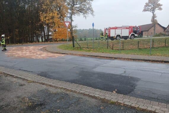 Einsatzkräfte der Feuerwehr beseitigen eine Ölspur auf der Bundesstraße, warnen Autofahrer.