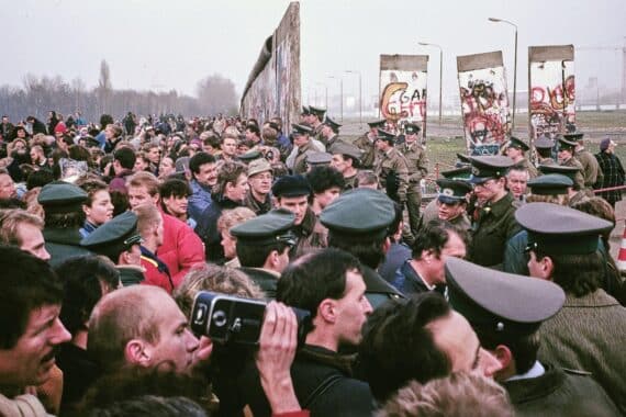 Bild einer Mauer mit Menschen, symbolisiert den Mut und die Hoffnung beim Mauerfall 1989.