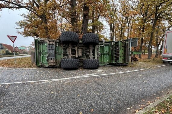 Unfall mit landwirtschaftlichem Anhänger: umgekippt, beschädigter Baum und gesperrte Kreuzung.