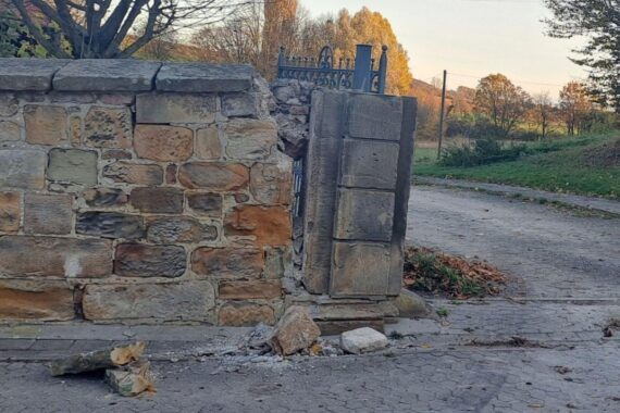 Beschädigte historische Steinmauer, Teile liegen verstreut, Polizei sucht Unfallverursacher.