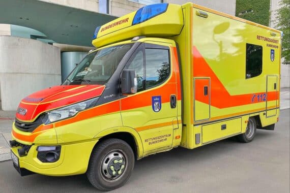 Rettungswagen am Unfallort mit beschädigten Fahrzeugen und Polizei, Verletzte werden versorgt.