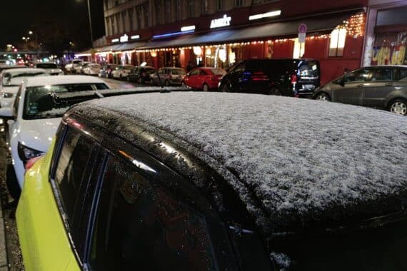 Winterliche Landschaft mit Schneefall, bedecktem Himmel und Autos mit Schnee auf dem Dach.