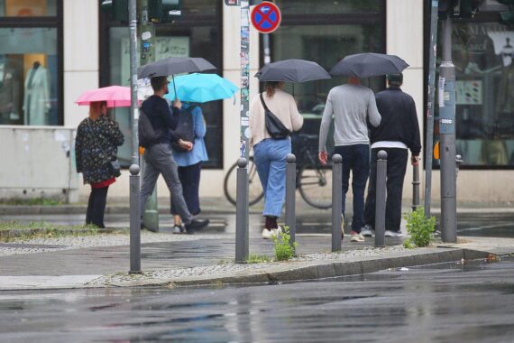 Regnerischer Tag in Niedersachsen: Menschen mit Regenschirmen bei starkem Wind und bewölktem Himmel.