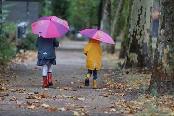 Zwei Kleinkinder genießen den Herbst, umgeben von buntem Laub und dichten Wolken.