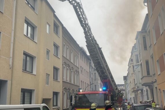 Feuerwehrkräfte löschen Küchenbrand in unbewohnbarer Wohnung, Rauch dringt aus mehreren Fenstern.