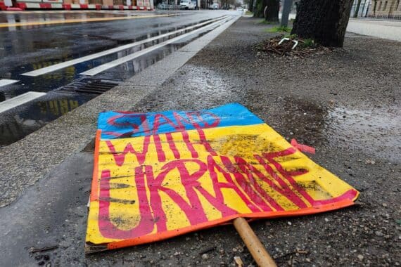 Ein Schild "Stand with Ukraine" liegt auf dem Boden, symbolisiert Solidarität und Unterstützung.