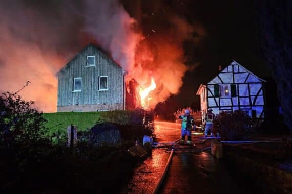 Ein brennendes Fachwerkhaus mit Feuerwehrkräften und Löschfahrzeugen im Einsatz.