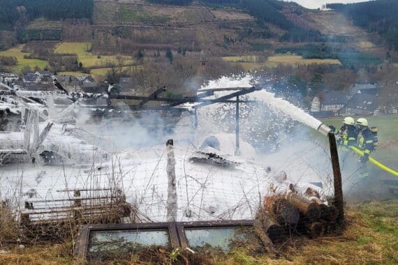 Scheune in Flammen, Feuerwehr im Einsatz, Traktor und Stroh betroffen, Rauch und Löschfahrzeuge sichtbar.