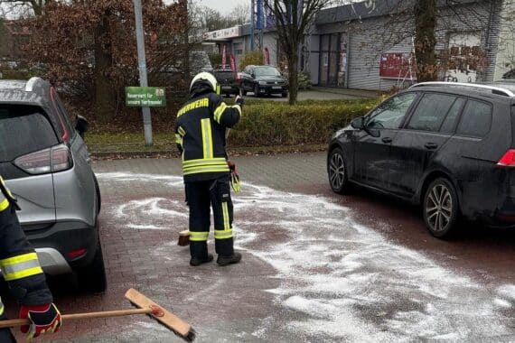 Feuerwehrleute streuen Bindemittel auf Parkplatz, um Ölfilm und Umweltschaden zu verhindern.