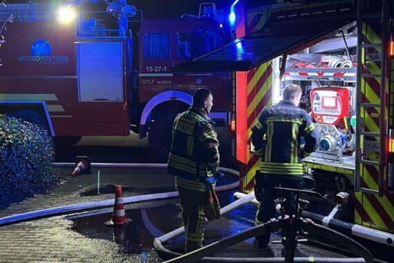 Großbrand auf Flugplatz: Zerstörte Hallen, Flugzeuge und Feuerwehr im Einsatz bei Nacht.
