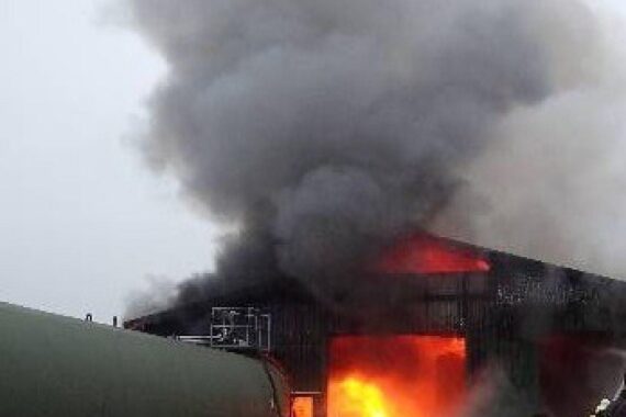 Brand in Lagerhalle: Feuerwehr im Einsatz, rauchende Trümmer und drohende Einsturzgefahr sichtbar.