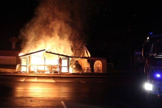 Abgebrannter Imbiss auf Parkplatz, Feuerwehr löscht, keine Verletzten, Polizei ermittelt Brandursache.