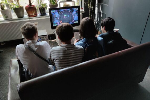 Junge Menschen spielen Videospiele, symbolisieren Freizeit, während wirtschaftliche Herausforderungen im Hintergrund bestehen.