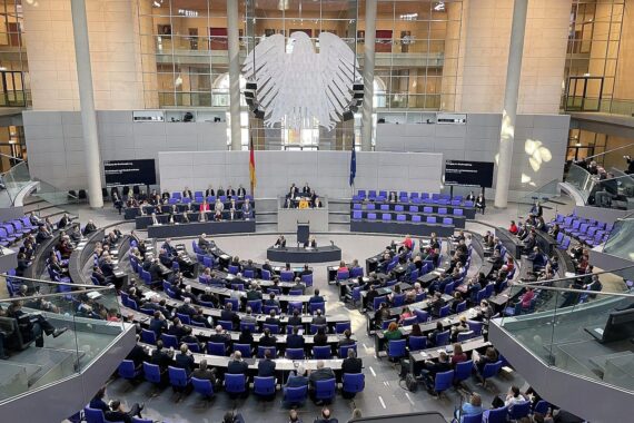 Bundestagssitzung mit Abgeordneten, die diskutieren, protestieren und aufeinander reagieren; viel Emotion.