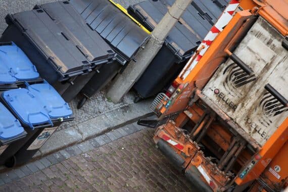 Müllabfuhrfahrzeug vor Stadtlandschaft, symbolisiert Gebührenerhöhungen und Umweltbewusstsein in Köln.