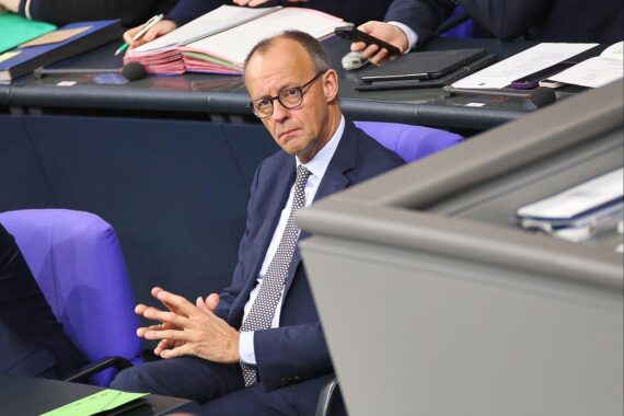 Heidi Reichinnek diskutiert Rentenreform im Bundestag, während Friedrich Merz im Hintergrund steht.