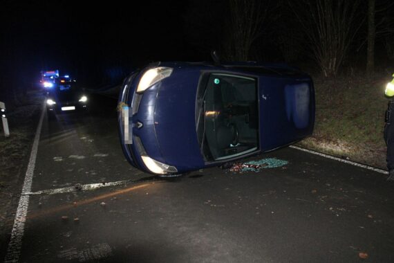 Unfallauto auf glatter Fahrbahn, umgekippt, Rettungsdienst im Einsatz, beschädigte Winterreifen sichtbar.