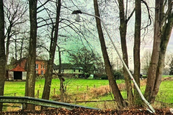 Unfallort mit beschädigter Straßenlaterne und grünen Lackspuren; Polizei sucht Zeugen für flüchtiges Fahrzeug.