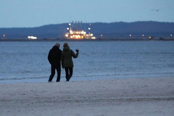 Paar spaziert am Strand unter wechselhaftem Himmel mit kaltem Wind und frostigen Temperaturen.