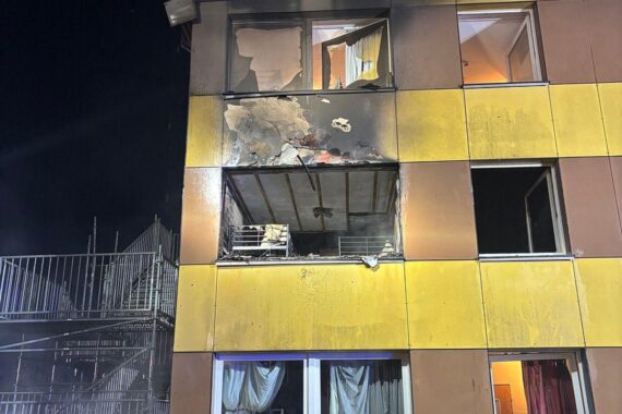 Zimmerbrand in Unterbringungseinrichtung: Feuerwehr im Einsatz, rauchende Trümmer, evakuierte Bewohner.