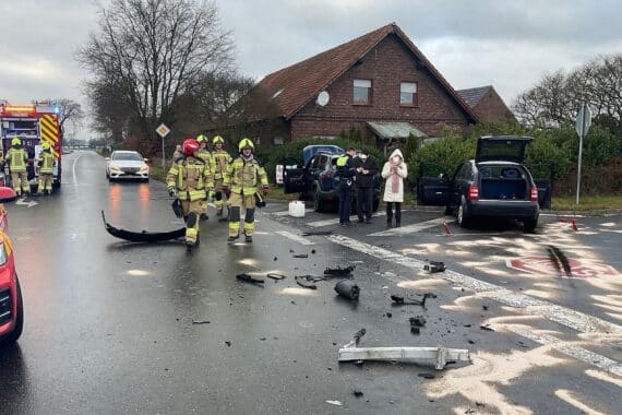 Unfallstelle mit beschädigten Autos, Feuerwehr im Einsatz, Verletzte Person, Absperrung der Straße.
