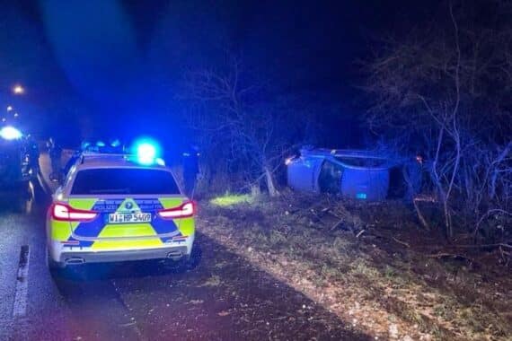Unfallstelle mit beschädigtem Mercedes im Gebüsch, Polizei vor Ort und Absperrungen.