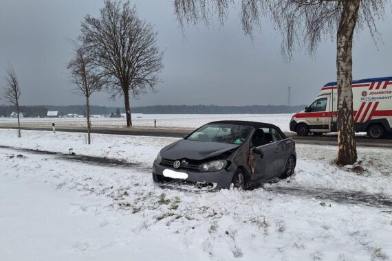 Ein Unfallfahrzeug am Baum, Feuerwehr und Rettungsdienst im Einsatz, gesperrte Straße.