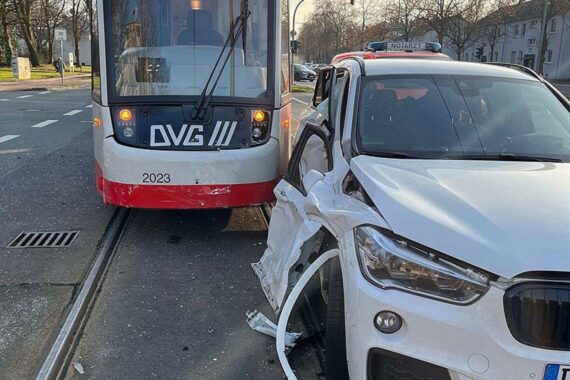 Unfallstelle mit beschädigtem weißem BMW und Einsatzkräften der Polizei und Feuerwehr in Duisburg.