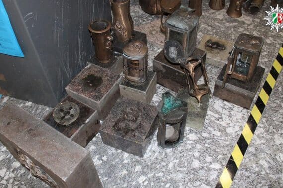 Drei Männer auf Friedhof, gestohlenes Diebesgut wie Grablichter, Polizei im Einsatz.