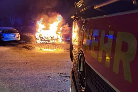 PKW brennt auf Parkplatz, Feuerwehr löscht, kein Personenschaden, Einsatzkräfte im Einsatz.