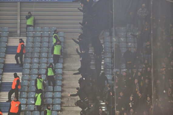 Aggressive Fans während eines Fußballspiels, Polizeikräfte im Einsatz, Chaos und Gewalt.
