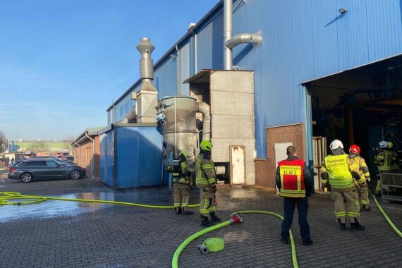 Einsatzkräfte löschen Brand in einer Absauganlage, Flammen schlagen aus dem Gerät.