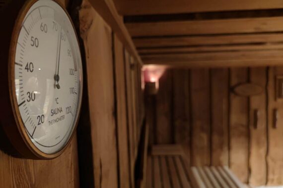 Ein Bild einer Sauna mit Menschen im Hintergrund und einem Smartphone, das heimlich filmt.