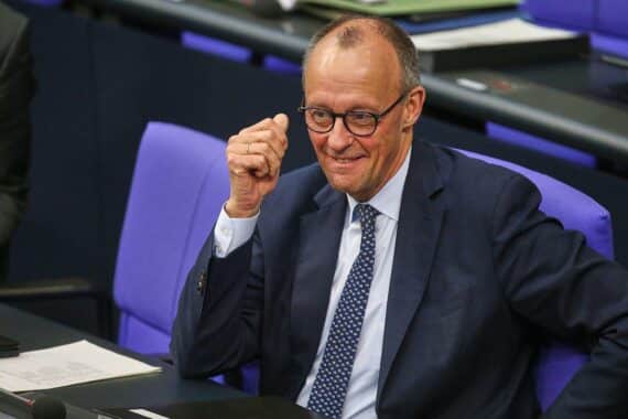 Friedrich Merz spricht vor Publikum, während politische Umfragen die Union und AfD zeigen.