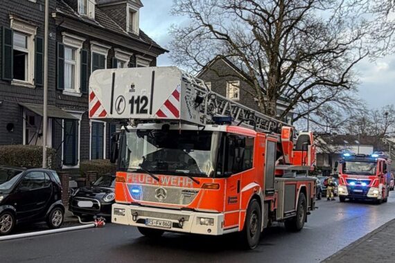 Feuerwehr löscht Küchenbrand in Mehrfamilienhaus; Rauch und Feuerschein sichtbar aus dem Fenster.